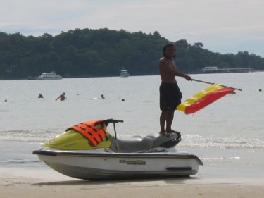 A jet-ski operator waves a lifeguard 'safe swimming zone' flag yesterday to recall a vehicle to Patong beach. Lifeguards say they need greater cooperation to save lives on Phuket beaches