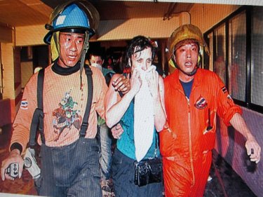Firemen help a tourist to safety amid last night's Bangkok fire