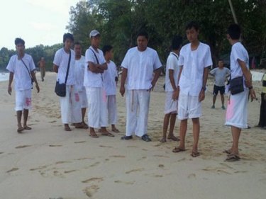 Onlookers, dressed in white for Phuket's Vegetarian Festival, stay back from the body found at Surin beach today. The woman's wrists were bound