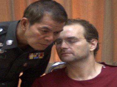 Ronald Fanelli whispers to a policeman at Phuket City police station