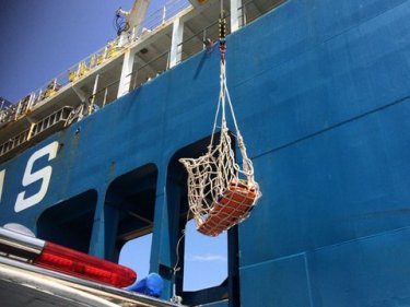 The heart attack victim's body is loaded over the side of the ship today